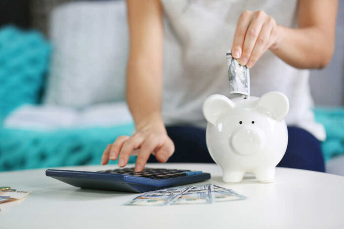 Female,Hand,Putting,Money,Into,Piggy,Bank,And,Counting,On