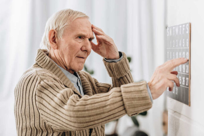 Senior,Man,Looking,At,Wall,Calendar,And,Touching,Head