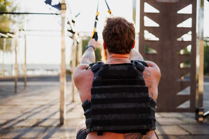 Back,View,Of,Sportsman,In,Weighted,Vest,Training,With,Suspension